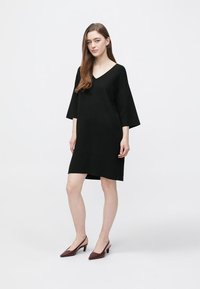 Black oversized V-neck dress with three-quarter sleeves, made of smooth fabric, features a straight cut and knee-length hem.