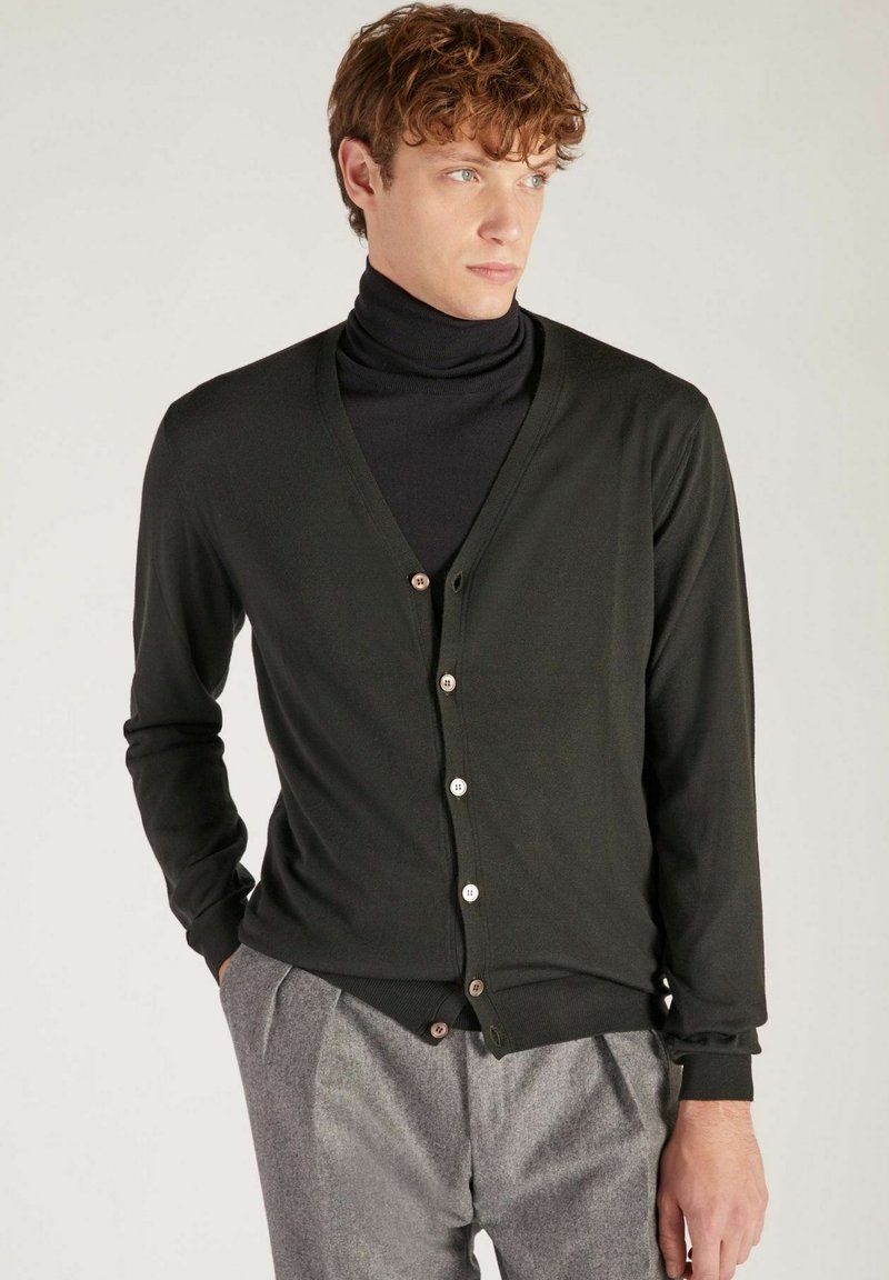 Cardigan noir avec un col en V et des boutons, doté de manches longues et d'une texture lisse, associé à un col roulé noir en dessous.
