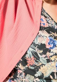 Coral-textured fabric top with button details, layered over a black floral print shirt featuring pink and blue flowers and green accents.