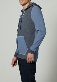 Sudadera con capucha en tonos azules, con un bolsillo frontal, mangas en contraste y cordón ajustable. Fabricada con un tejido suave y texturizado.