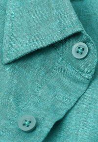 Turquoise linnen stof met een gestructureerd oppervlak en een opgestikte kraag. Bevat bijpassende knopen met een ontwerp van vier gaten.