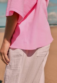 Tricou cu mânecă scurtă, roz deschis, cu croială lejeră, asortat cu pantaloni din in bej deschis, cu buzunare laterale și material texturat.