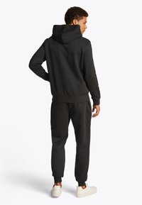 Black sweatshirt with a hood, ribbed cuffs, and hem, paired with matching joggers. Smooth texture, minimal design, worn with white sneakers.
