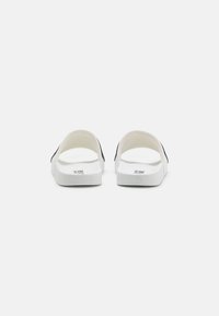 White sandals with a smooth texture and open back, featuring a contrasting black accent on the side and a textured sole for grip.