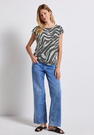 Blusa ligera de manga corta con un patrón de rayas de cebra en verde y blanco, combinada con unos pantalones vaqueros de pierna ancha en azul claro y unas sandalias negras tipo slide.