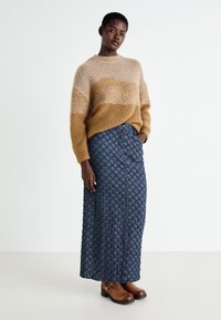 Beige och brun randig stickad tröja i kombination med en lång, strukturerad marinblå kjol med diamantmönster samt bruna ankelboots.