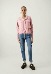 Ροζ βελουτέ μπουφάν με κουμπιά και δύο μπροστινές τσέπες, συνδυασμένο με ανοιχτό μπλε τζιν και σκούρες καφέ πλατφόρμες. Λευκές κάλτσες είναι ορατές.