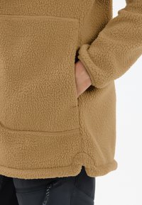 Beiger Fleece-Pullover mit strukturiertem Außenmaterial, großer Fronttasche und verlängerten Bündchen. Der untere Saum ist abgerundet für zusätzlichen Komfort.