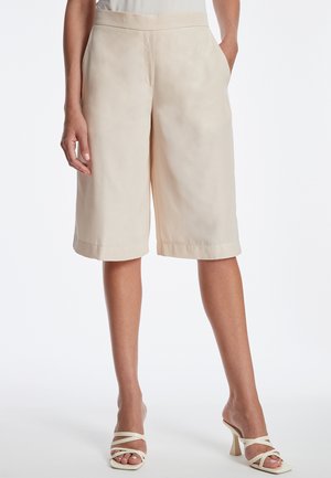Culottes beiges en tissu léger, avec une texture lisse, des poches latérales et une coupe détendue, à la longueur légèrement raccourcie.