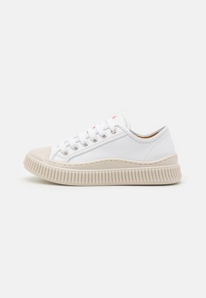 Sneaker bianca in pelle con punta arrotondata, cuciture tono su tono e una suola in gomma beige spessa con scanalature orizzontali e dettagli.