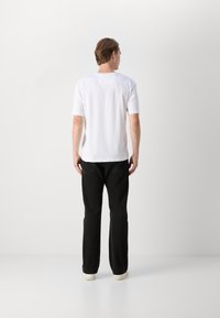 Hvit t-skjorte med korte ermer og rund hals, i en avslappet passform, kombinert med svarte jeans med rette ben og hvite joggesko.