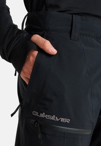 Schwarze Stoffhosen mit einer seitlichen Tasche mit Reißverschluss und Logo. Enthält einen Daumenlochsaum und einen verstellbaren Bund.