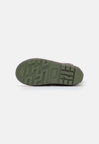 Semelle de chaussure en caoutchouc verte avec un motif de semelle texturé, présentant un design en relief et des bords renforcés pour la durabilité.