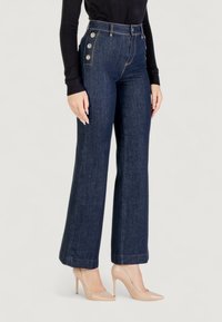 Jeans a vita alta blu scuro con gamba svasata, dotati di dettagli con bottoni dorati sul davanti e cuciture a contrasto. Tessuto denim liscio.