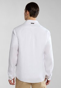 Camicia bianca a maniche lunghe realizzata in tessuto leggero, caratterizzata da un colletto classico, chiusura con bottoni e una piega sul retro per facilitare il movimento.