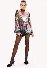 Rompers à sequins avec manches longues, col montant et motif irisé multicolore. Short noir avec ourlet volants. Fini avec des talons noirs.