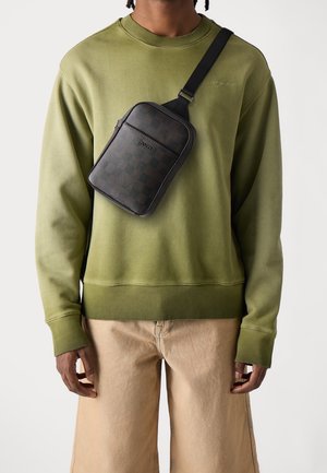 Mustat ruudulliset rintalaukun, jossa on vetoketjullinen etutasku, säädettävä hihna, käytetään oliivinvihreän collegepaidan sekä beigejen löysälahkeisten housujen kanssa.