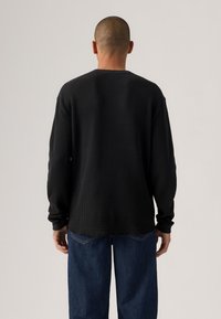 Black ribbed long-sleeve shirt with a relaxed fit, featuring a crew neckline and rolled sleeves, worn over blue denim pants.