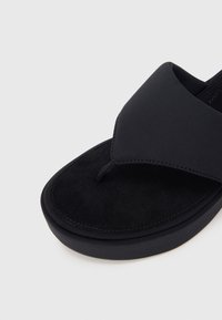 Μαύρο παντοφλάκι με μαλακό πάνω λουρί, υφασμένο συνθετικό πάτο από σουέτ, στρογγυλή υποστήριξη  δακτύλων και ανθεκτική ελαστική σόλα με ραφές.