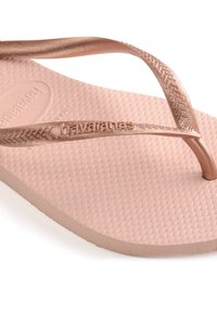 Rosa gull flip-flop med flat, teksturert gummisåle. Stropper er metalliske og slanke, med preget merkevare. Uformell design.