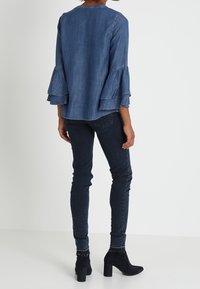 Top in denim blu con maniche a campana a strati, abbinato a jeans slim-fit scuri e stivali neri alla caviglia. Texture liscia, design casual.