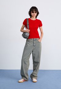 Red ribbed knit short-sleeve top with a white neckline, paired with loose light blue denim jeans and white sneakers with red stripes.