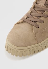Baskets en suede beige avec lacets plats, accents cousus, bout rond et semelle rugged crantée. Texture lisse et design discret.