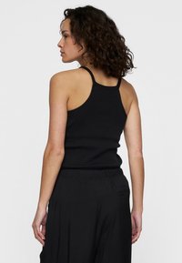 Zwarte geribde tanktop met dunne bandjes, met een aansluitende pasvorm. De stof heeft een gladde textuur, gecombineerd met zwarte losse broek.