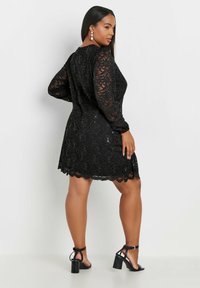 Musta pitsimekko pitkähihaisena, aaltoilevalla helmalla ja strasseilla koristeltuna. Yhdistetty mustiin remmissandaaleihin.