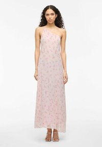 Maxi dress in sheer, light pink fabric with small floral print. Features a one-shoulder design and flowing silhouette. Silver strappy sandals.