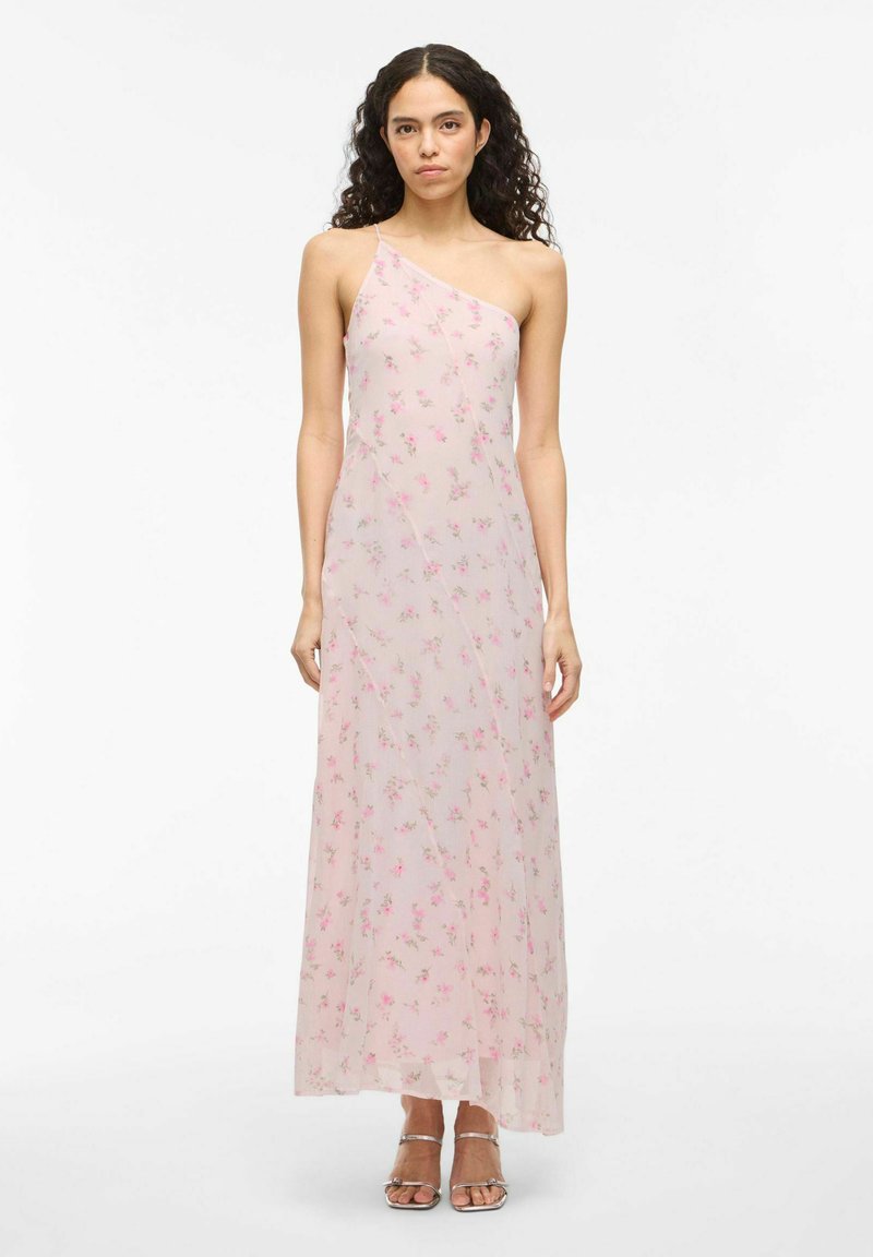 Maxi dress in sheer, light pink fabric with small floral print. Features a one-shoulder design and flowing silhouette. Silver strappy sandals.