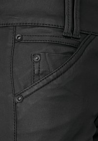 Pantalons en denim noir avec une poche avant dotée d'un bouton visible et de coutures détaillées. La texture semble lisse avec un léger éclat.