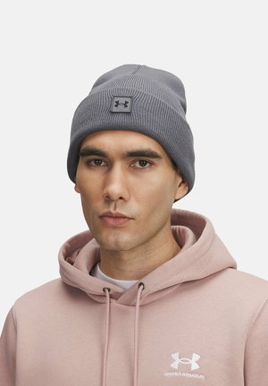 Gray knitted beanie with a textured finish and a logo patch, worn with a light pink hooded sweatshirt featuring a white logo.