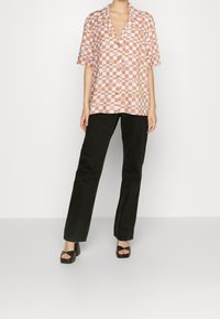 Short-sleeve, checked patterned shirt in peach and blue, paired with black straight-leg trousers and black platform sandals. Gold button detail.