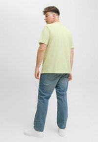 Helles grünes Baumwoll-T-Shirt mit kurzen Ärmeln, rundem Halsausschnitt und lässiger Passform; getragen mit lockeren blauen Jeans und weißen Turnschuhen.