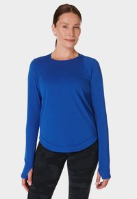 Langarmige blauwe sporttop met een afgeronde zoom, gemaakt van lichte stof, met raglanmouwen en een soepele textuur.