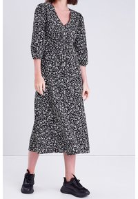 Robe midi noire à fleurs avec un décolleté en V et des manches trois-quarts, dotée d'une taille froncée et portée avec des baskets noires.