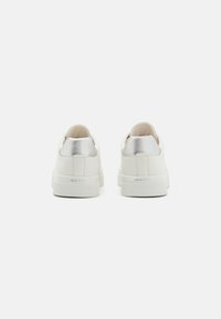 White sneakers with a smooth leather upper and a metallic silver heel tab. Features a textured rubber sole and embossed branding on the heel.