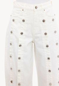 Pantalon blanc taille haute avec plusieurs rangées verticales de boutons pression argentés et poches avant visibles.