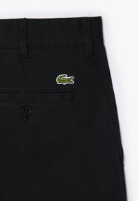 Zwarte katoenen broeken met een groen geborduurd krokodillogo, voorkant van de tailleband met riemlussen en een knoopsluiting.