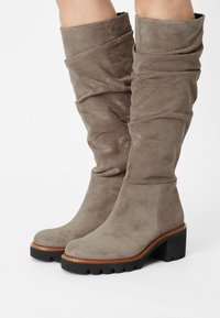 Botas de ante taupe hasta la rodilla con cañas holgadas, punteras redondeadas, ribetes marrones y suelas de goma negra gruesas con tacones en bloque.