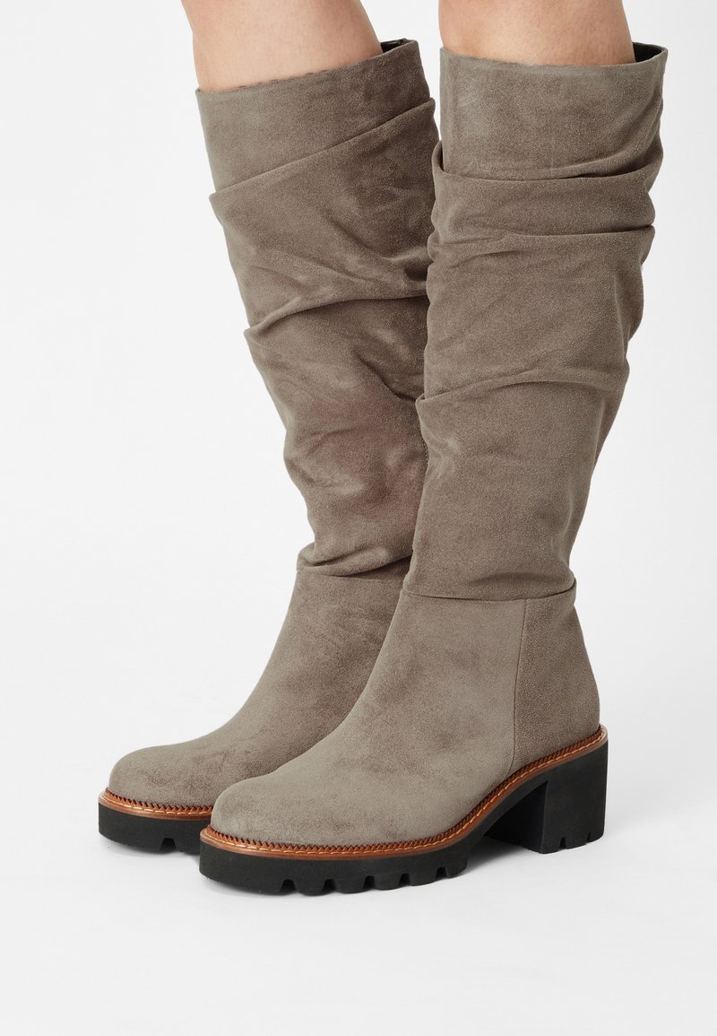 Botas de ante taupe hasta la rodilla con cañas holgadas, punteras redondeadas, ribetes marrones y suelas de goma negra gruesas con tacones en bloque.