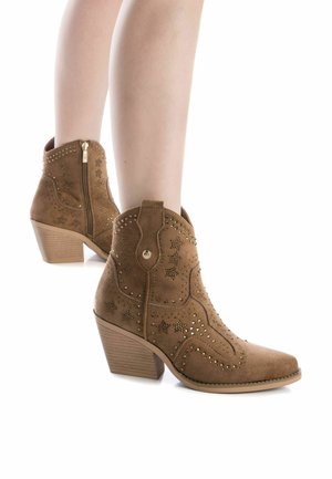 Botas de vaquero de ante en color marrón claro con punta afilada, detalles de costura, acentos metálicos y un tacón apilado de 6.5 cm; funcionalidad de cremallera lateral.