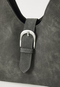 Sac à main en cuir synthétique gris avec un accent de boucle en argent et des détails de couture visibles. La surface a une finition texturée et vieillie.