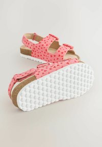 Sandali rosa con piccolo motivo a cuori, cinturini regolabili e lati aperti. Suola interna in sughero e suola in gomma bianca testurizzata per una buona presa.