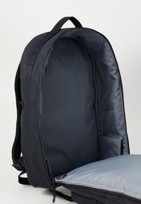 Sac à dos en tissu noir avec un intérieur gris lisse et spacieux. Comprend une fermeture éclair, une section rembourrée et des poches latérales pour le rangement.