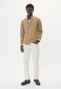 Svetlohnedá košeľa s gombíkmi a hladkou textúrou, kombinovaná s bielymi nohavicami a čiernymi topánkami. Jednoduchý dizajn, dlhé rukávy a klasický golier.