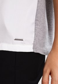 Top de manga corta con el frente blanco y la parte trasera gris, hecho de una tela suave con un elegante detalle de etiqueta en el dobladillo.