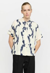 Kurzärmlige Bluse aus cremefarbenem Stoff mit einem marineblauen Blumenmuster, einem Hemdkragen und einem lässigen Schnitt. Glatte Textur mit sichtbaren Nähten.