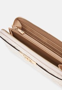 Portefeuille beige clair avec texture matelassée, quincaillerie dorée et fermeture à glissière. L'intérieur comprend plusieurs emplacements pour cartes et une poche zippée.